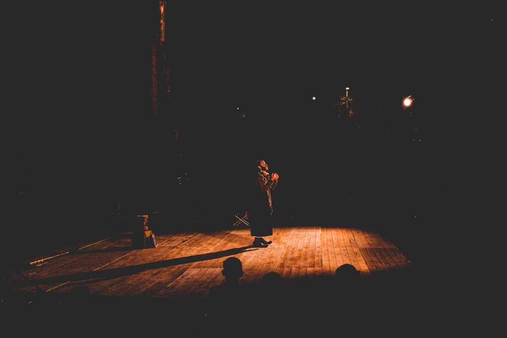 A single, dimly lit performer on a theater stage.